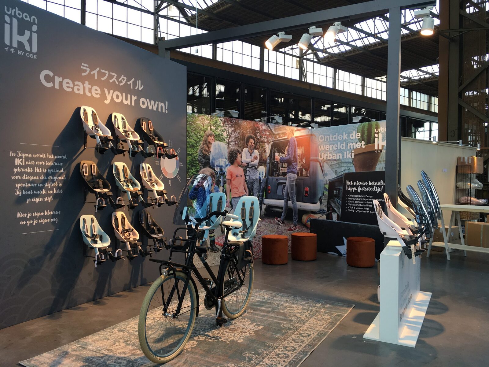 Beursstand van Urban Iki met een wand vol fietsstoeltjes en een fiets op een kleed